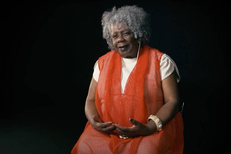 Imagem representando uma mulher negra sentada com as mãos no colo
