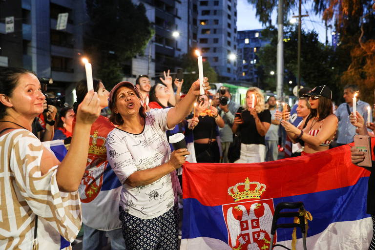 Mulheres reunidas com velas e uma bandeira da Sérvia