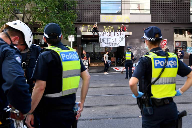 Policiais observam manifestantes com cartazes em frente a prédio