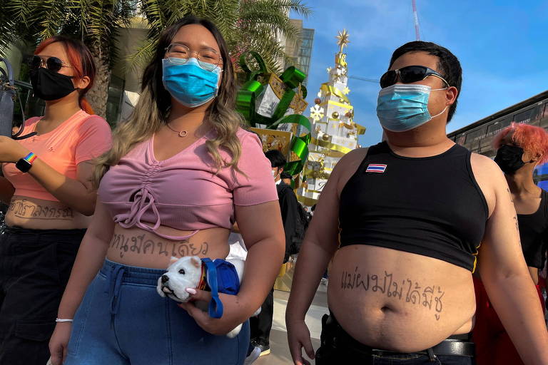 Mulher e homem de crop-top e máscara, com mensagens de protesto escritas na barriga