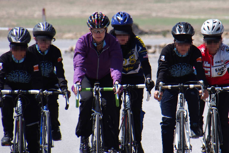 Com uniforme preto e hijab, 6 ciclistas pedalam em estrada