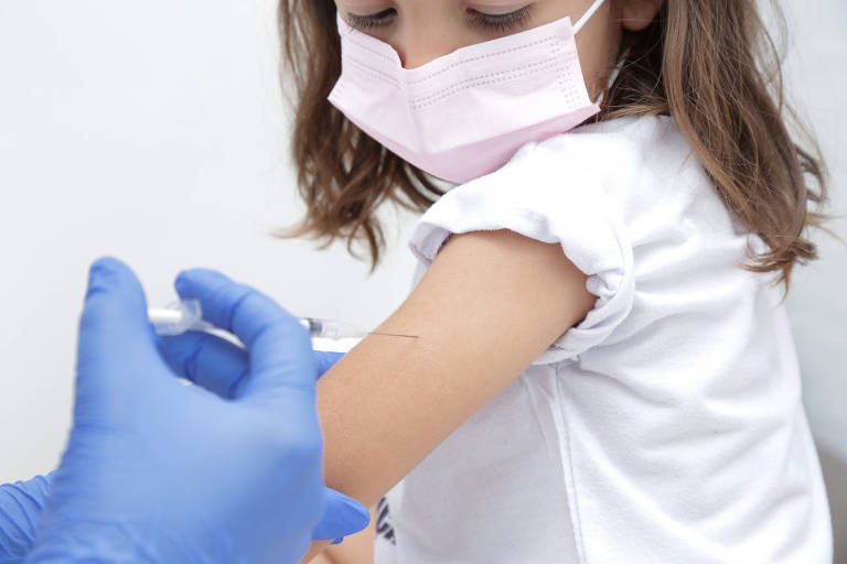 Criança de máscara rosa toma injeção no braço