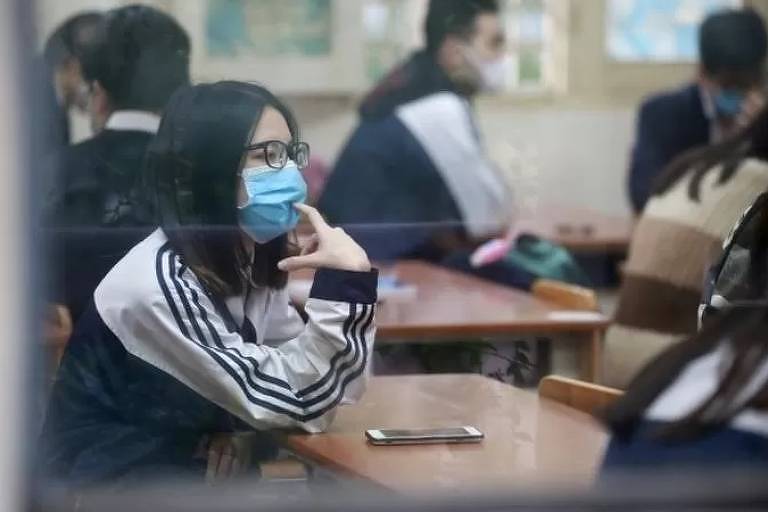 Imagem em primeiro plano mostra adolescente de máscara sentada em uma carteira escolar