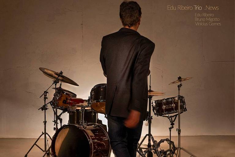 Em foto colorida, o baterista Edu Ribeiro aparece de costas caminhando para a bateria
