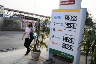 A woman passes by a price board at a gas station in Rio de Janeiro