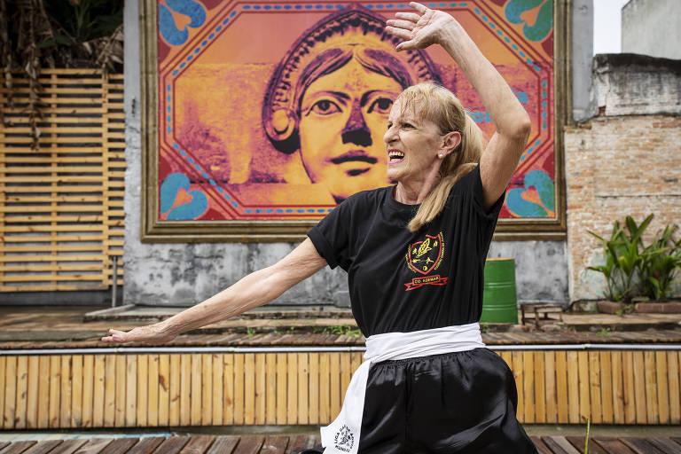Mulher de cabelos brancos e soltos, vestida com roupa preta de kung fu, faz movimentos da luta arte marcial na Vila Itororó