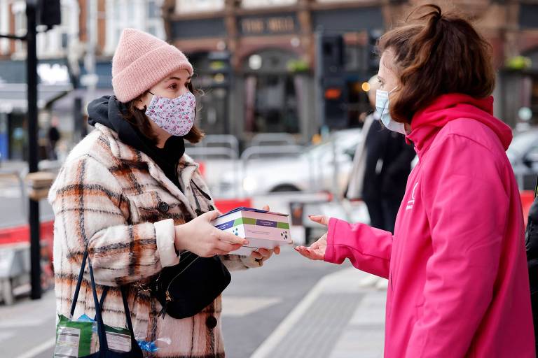Pessoa vestida de rosa entrega caixa de testes para mulher que passa pela rua