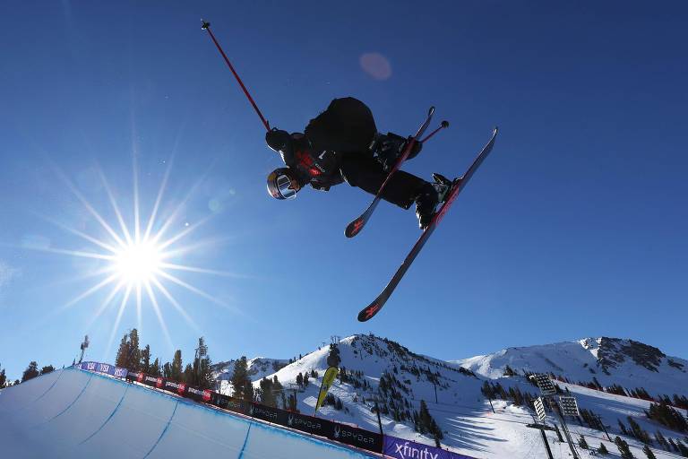 Esquiadora faz manobra no ar em meio ao céu azul e à pista de neve