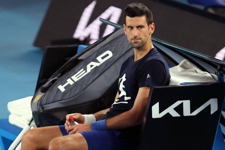 Djokovic sentado em banco em quadra de tênis com expressão séria 