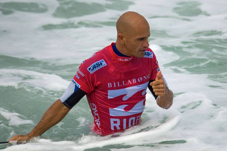 Surfiat careca, de camisa vermelha, está praticando o esporte no mar
