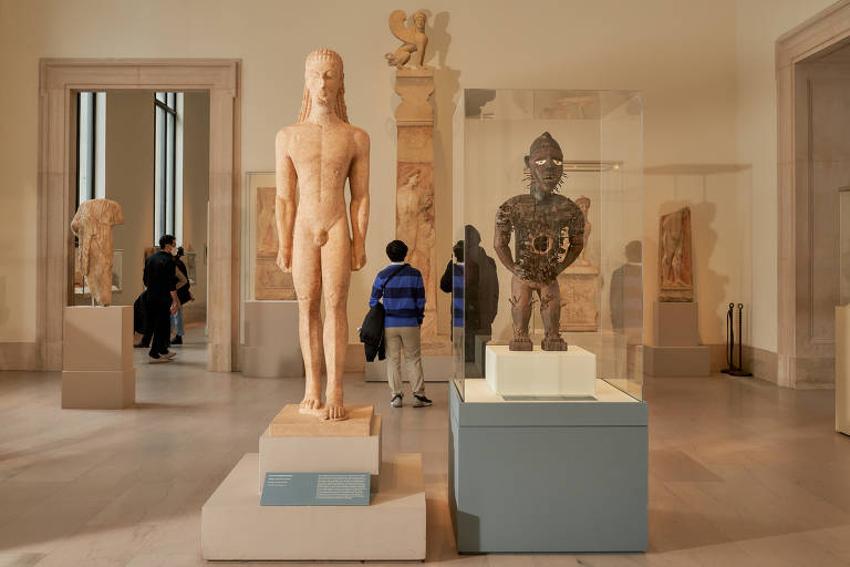 Sala de museu que mostra à esquerda uma estátua branca, de um homem nu, que é a grega, e à direita, uma estátua menor, em material marrom escuro, que é a de etnia kongo, também em forma de homem