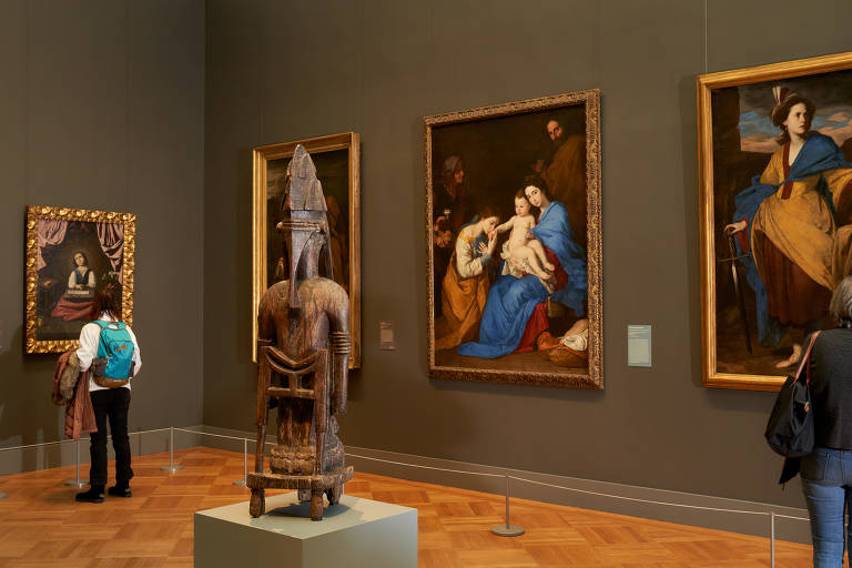 Visão geral de sala do museu mostra o diálogo entre as peças escolhidas da coleção de arte africana e as pinturas de arte clássica europeia nas paredes