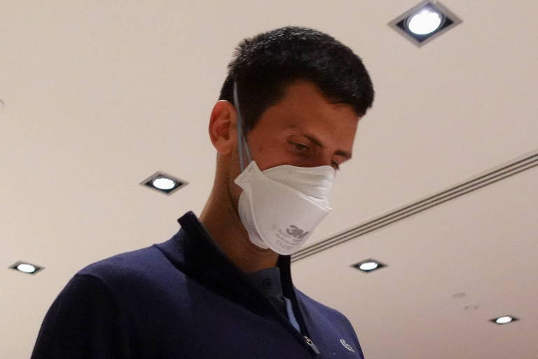 Djokovic caminha de cabeça baixa e com máscara e facial