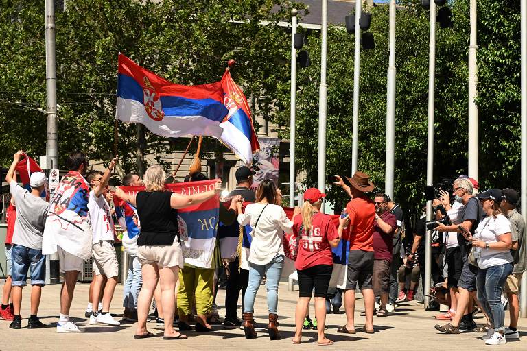 Cerca de 15 pessoas com bandeira da Sérvia em frente a prédio