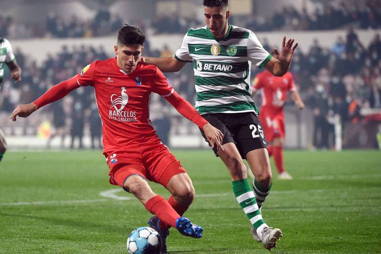 O atacante espanhol Fran Navarro, do Gil Vicente, domina a bola em partida contra o Sporting; seu uniforme é vermelho e há um adversário perto dele, com camisa com listras horizontais nas cores em verde e branco