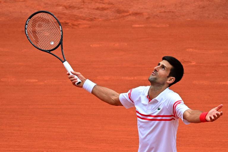 Djokovic com os braços abertos e olhando para cima, em postura de descontentamento na quadra de saibro