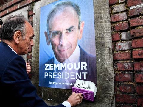 TOPSHOT - French far-right party Reconquete! presidential candidate Eric Zemmour glues a campaign poster on a wall during a campaign visit in the northern France village of Honnecourt-sur-Escaut on January 14, 2022. (Photo by BERTRAND GUAY / AFP)