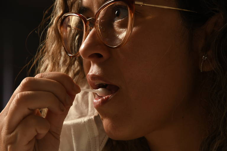 Mulher usando óculos introduz cotonete na boca