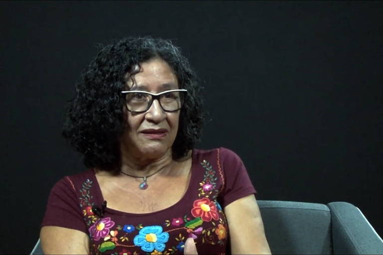 Mulher de óculos dá entrevista com fundo preto