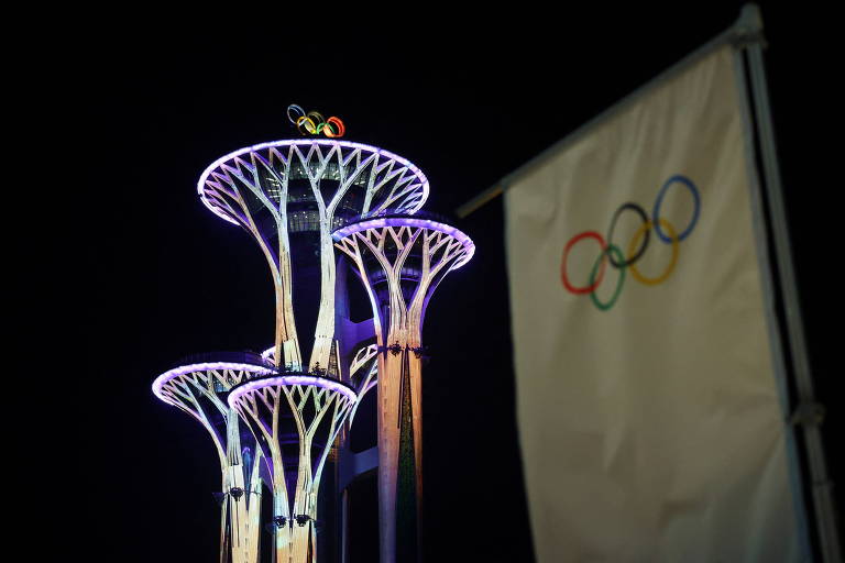 Torre iluminada ao lado de bandeira com os anéis olímpicos