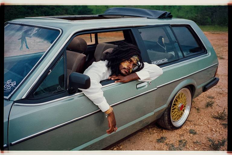 Em foto colorida o cantor, compositor e rapper Rico Dalasam posa para a câmera dentro de um carro com os braços para fora da janela