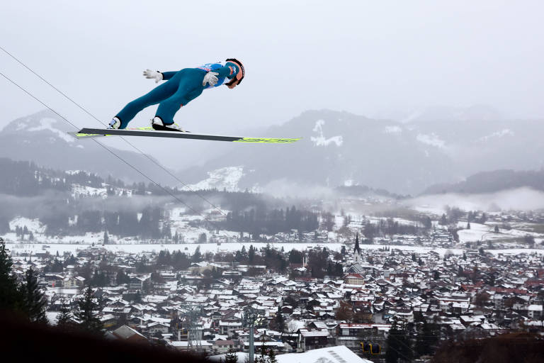 Esquiador suspenso no ar acima de vilarejo coberto de neve