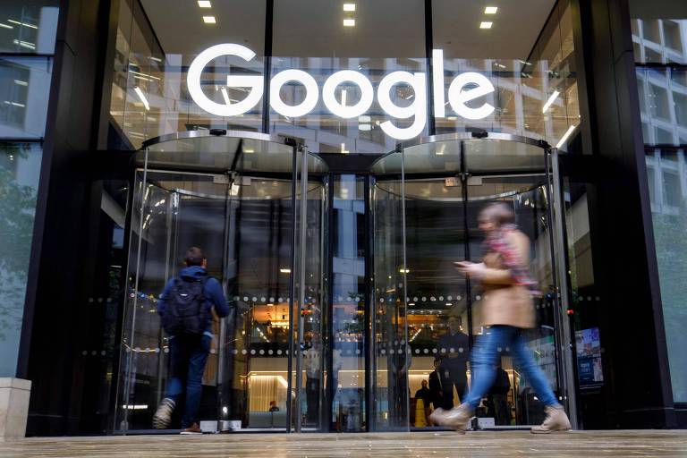Pessoa com roupa de frio caminha em frente a porta giratória de vidro com o logo do Google
