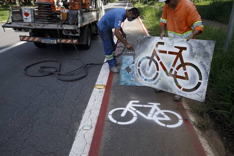 Operários pintam desenho de bicicleta no asfalto da ciclovia