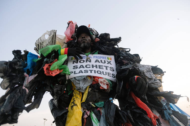Modou Fall, who works to educate fellow Senegalase residents about the dangers of plastic trash, holds a sign reading Òno to plastic bagsÓ as he makes his case at the annual marathon in Dakar, Senegal, on Nov. 21, 2021. Dressed head to toe in plastic, Modou Fall is a familiar sight in Dakar. (Ricci Shryock/The New York Times)