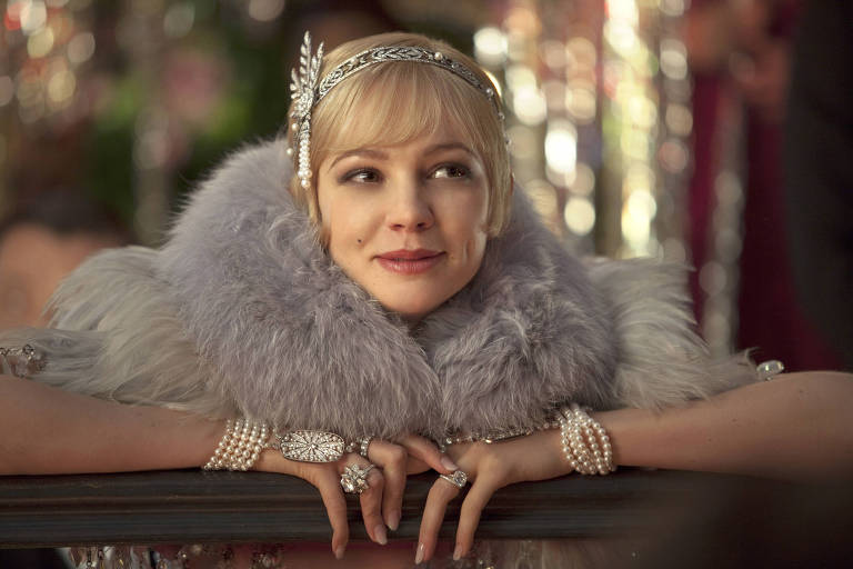 Mulher jovem loira usa um felpudo casaco lilás, joias de pérola lilás e uma tiara de prata 