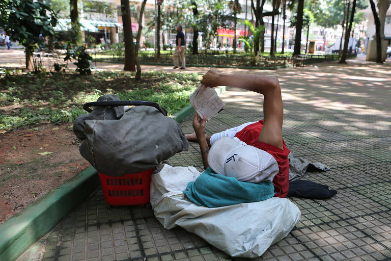 Homem deitado no chão da praça Dom José Gaspar, no centro de São Paulo, faz palavra cruzada