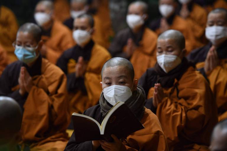 Em filas, monges de túnicas alaranjadas oram usando máscaras de proteção contra a Covid-19