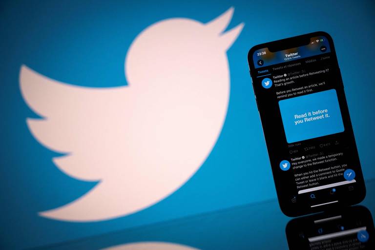 Ao fundo, tela com logo do twitter que tem fundo azul e ao centro um pássaro branco, à frente um celular mostra postagens na rede social