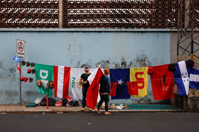 Bandeiras de partidos políticos em rua de Tegucigalpa, a capital de Honduras; elas estão em um varal, na calçada, à frente de um muro