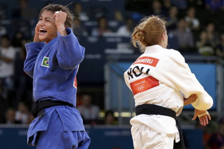 Sarah Menezes, de quimono azul, ergue os braços e comemora vitória sobre rival de quimono branco