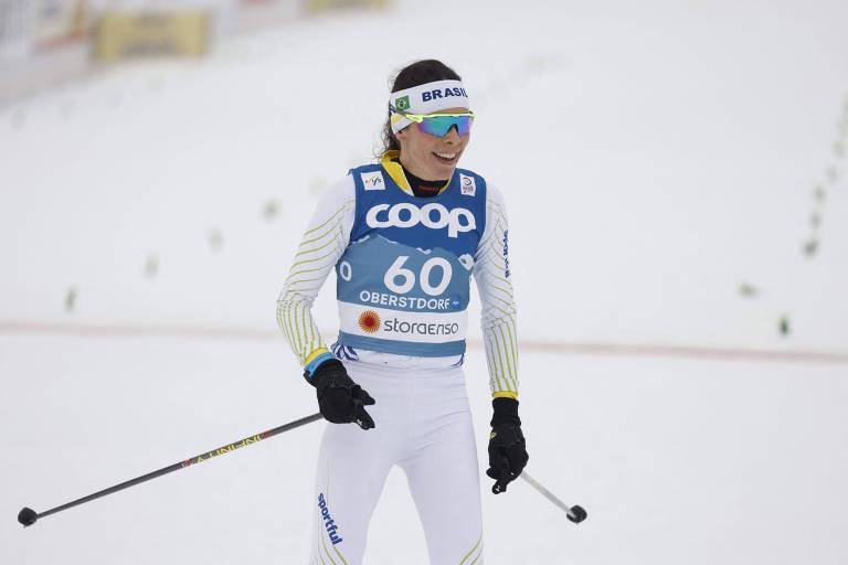 Jaqueline com roupa de esqui, bastões nas mãos e óculos protetor na neve