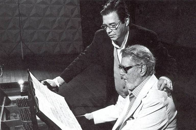 Em foto preto e branco aparece ao piano o maestro Radamés Gnattali, e em pé, o maestro Tom Jobim, com sua mão sobre o ombro do amigo