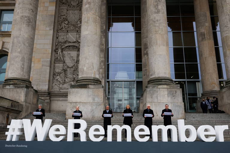 Autoridades posam para foto em frente ao prédio da parlamento alemão com totem em homenagem às vítimas do Holocausto com os dizere #NósLembramos em Berlim