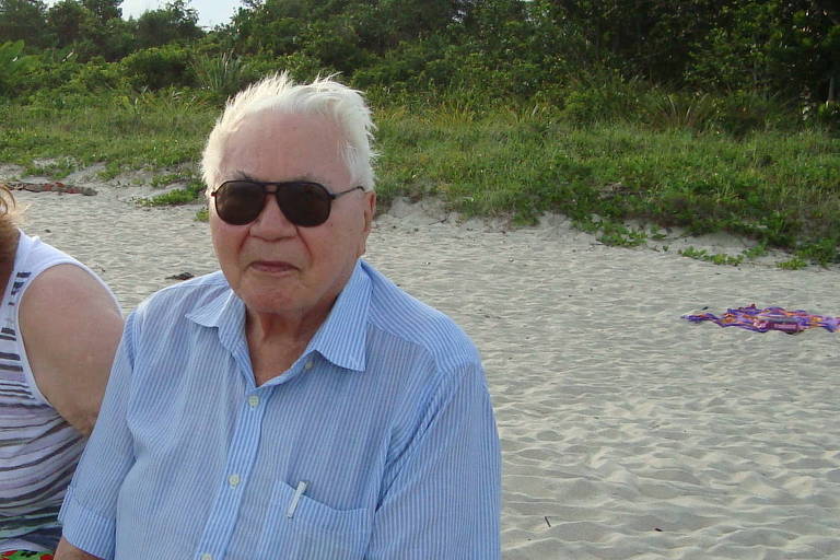 Homem idoso ao lado de uma mulher sentado na praia