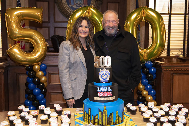 Duas pessoas sorriem em uma festa. Atrás deles há balões escrevendo o número 500 e em frente a eles há uma mesa com docinhos e um bolo onde se lê "500" e "Law & Order: Special Victims Unit"