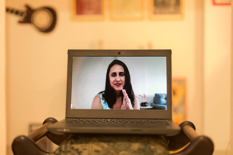 Imagem de mulher é vista em tela de computador em frente a um fundo ocre