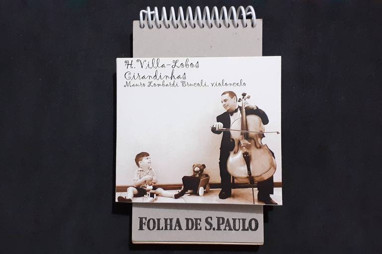 Em foto colorida, sobre um bloco da Folha, aparece a capa do álbum 'Villa-Lobos Cirandinhas', que traz na foto o violoncelista Mauro Brucoli tocando violoncelo enquanto seu filho pequeno brinca com brinquedos