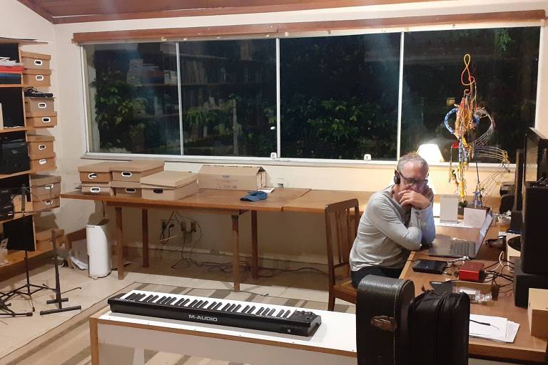 Em foto colorida, O compositor e arranjador Dante Ozzetti aparece sentado, diante de um computador, ouvindo o CD 'Valsas, Choros e Canções' de Eduardo Gudin, às cegas, em seu estúdio em São Paulo