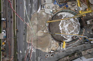 Cratera  que foi aberta ao lado de obra do metro na Marginal  Tiete (entre pontes do Piqueri e Freguesia do O) recebe concreto despejado por tubos ligado a  caminhoes