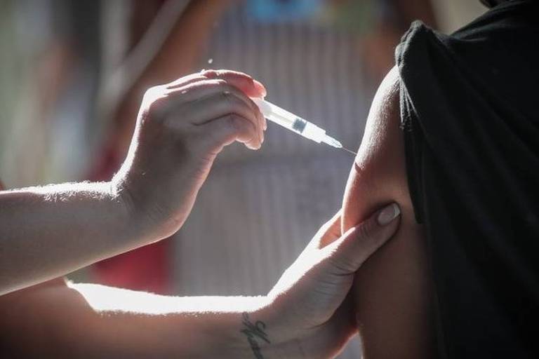 Imagem em close mostra uma pessoa aplicando vacina no braço de uma criança