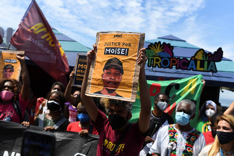 Manifestantes levantam cartazes com o rosto de Moïse em frente ao quiosque Tropicália