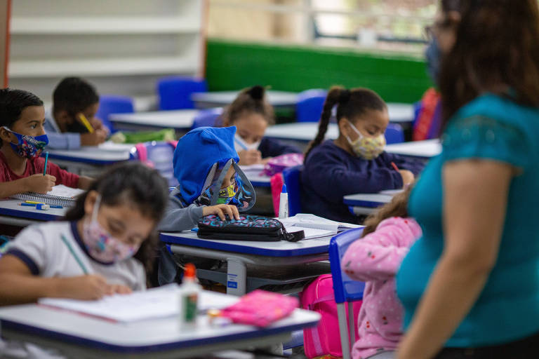 Crianças sentadas em carteiras escolares usando máscara de proteção no rosto