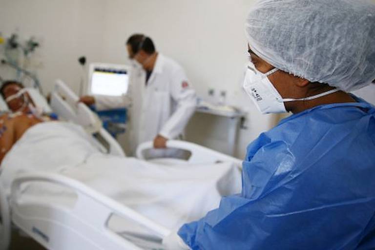 Imagem em primeiro plano mostra profissional da saúde olhando para paciente em uma maca de hospital