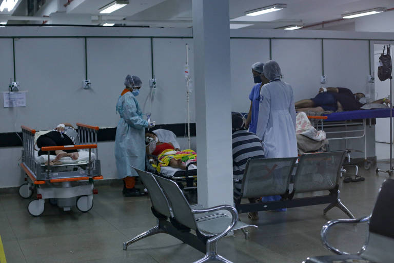 funcionários de hospital com jalecos e toucas brancas atendem paciente em macas