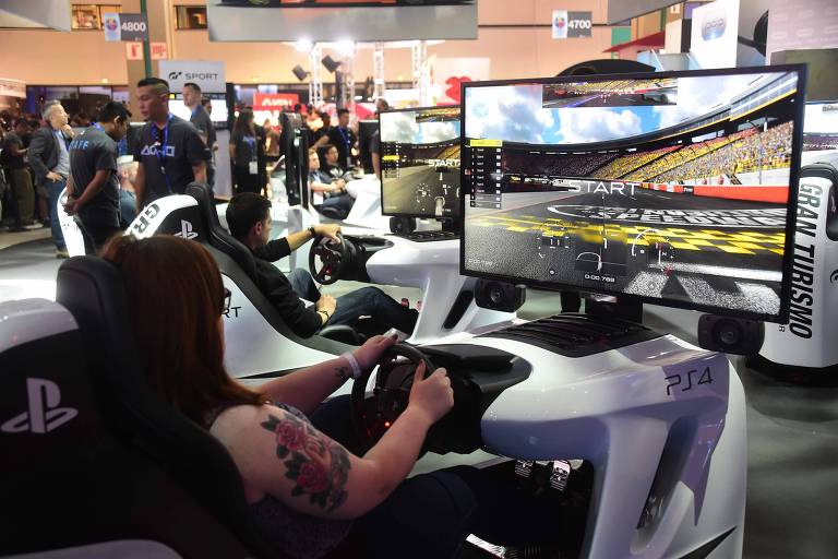 Mulher sentada em cabine de simulador de corrida para videogame, com jogo em tela 